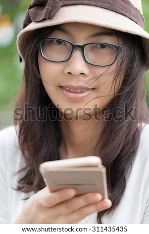asia woman use smart phone.joy and smile smart phone.wear hat and eyeglasses.