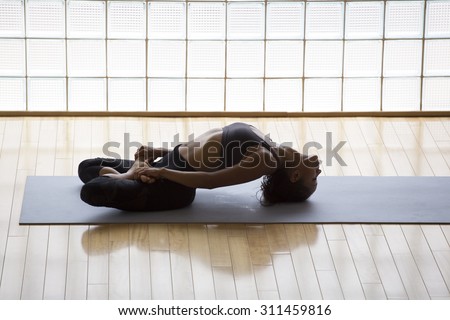 Above shot of a young woman practicing in a yoga studio. Fish pose, or Matsyasana with lotus legs.