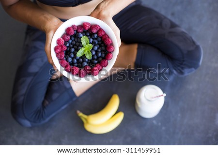 Above shot of a woman with a bowl of berries, a bottle of almond milk and two bananas wearing a sportive outfit. Royalty-Free Stock Photo #311459951