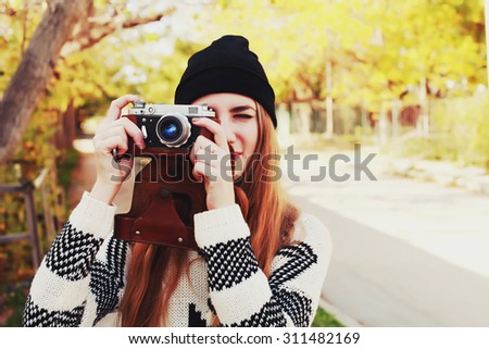Outdoor lifestyle portrait of pretty young hipster woman making photo. Retro photographer. Modern urban girl has fun with vintage photo camera. Photo toned style Instagram filters.