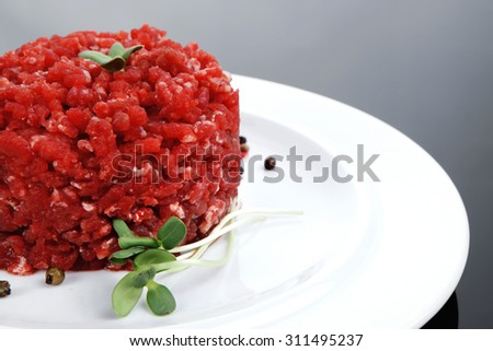 very big raw hamburger cutlet with sprouts and chilli pepper on white plate over black background