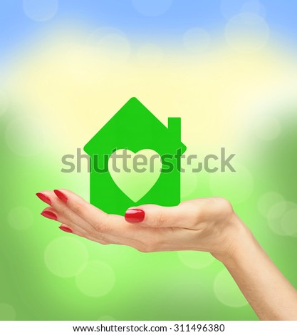 Female hand with small model of house over blurred nature background