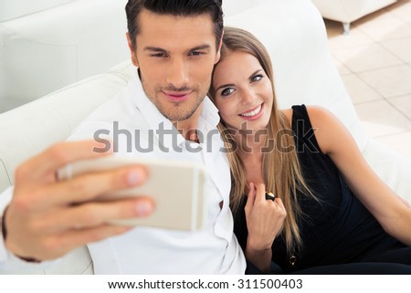 Smiling young couple making selfie photo on smartphone indoors
