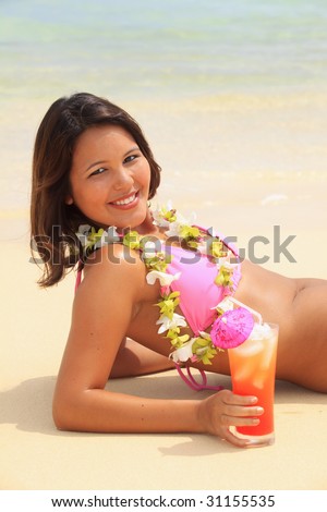  beautiful Polynesian girl with flower lei in a pink bikini lying on a secluded Hawaii beach while enjoying a tropical drink