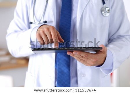 Male medicine doctor holding digital tablet pc and pointing it with finger. Medical equipment, modern technology and communication concept. Therapeutist using portable computer searching information