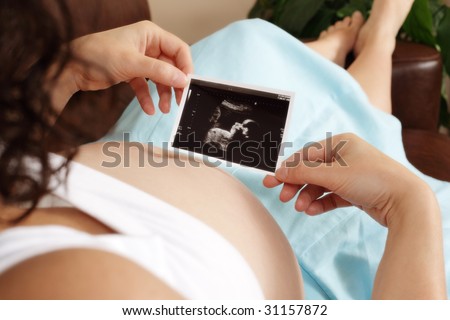 Pregnant woman sitting on sofa looking at her unborn baby's ultrasound scan Royalty-Free Stock Photo #31157872