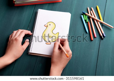 Female hands drawing duck in notebook on wooden table background