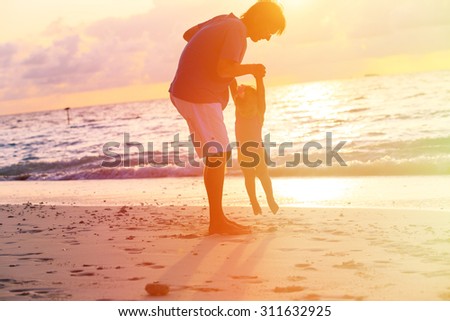 silhouettes of father and little daughter playing at sunset beach