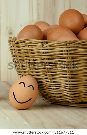 Smiling and happy egg lying against a wicker bucket of eggs
