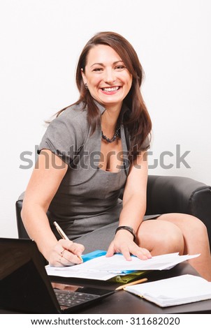 Smiling woman subscribing document while sitting on arm-chair by desk