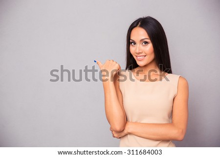 Portrait of a cheerful woman pointing finger away over gray background