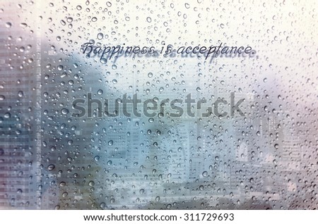 Waterdrops on a glass surface windows with Happiness is acceptance qoutes on cityscape background