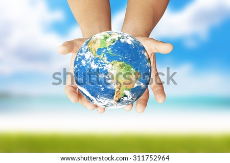 Male hands holding earth on blurred sea background with green grass floor: Green world: Elements of this image furnished by NASA