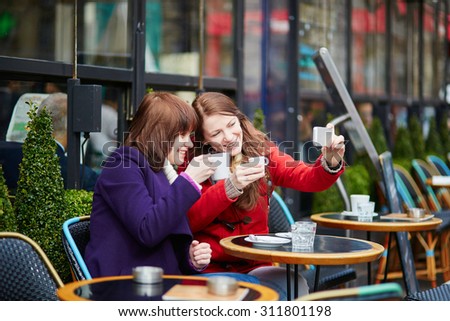 Two cheerful girls taking selfie in a Parisian street cafe