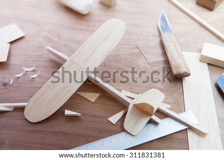 Making model airplane from wood. Wooden air plane handcrafted with balsa wood, on work table by the window. Airplane, knife, balsa wood material and glue on table. Shallow depth of field.