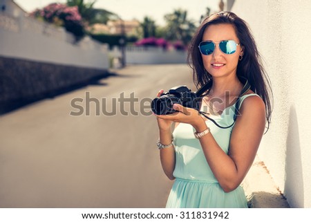 Portrait of a young, fit and attractive woman taking a photo outdoor. Posing on the street on a sunny summer day. Girl looking at the camera.