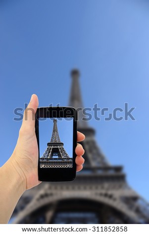 Woman taking photo of Eiffel Tower with cell phone.