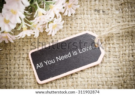 All you need is love vintage wood tag with flower on sack background.