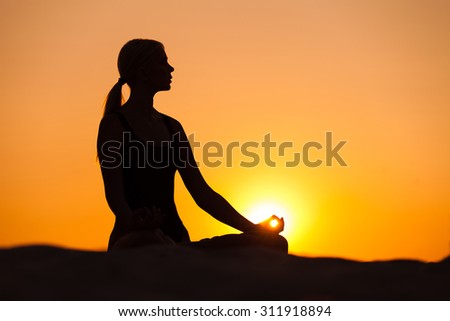 Silhouette young woman practicing yoga on sand at sunset
