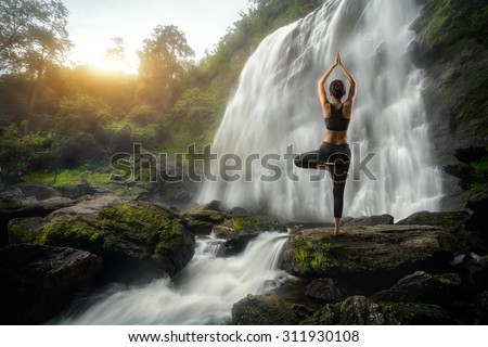 Young woman in a yoga pose at the waterfall