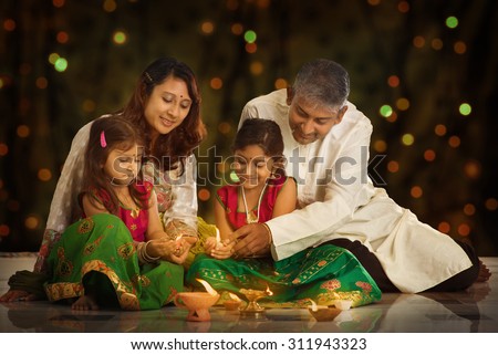 Indian family in traditional sari lighting oil lamp and celebrating Diwali or deepavali, fesitval of lights at home. Little girl hands holding oil lamp indoors. Royalty-Free Stock Photo #311943323