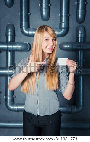 beautiful young smiling woman with blond long hair standing against PVC pipes construction holding empty business card
