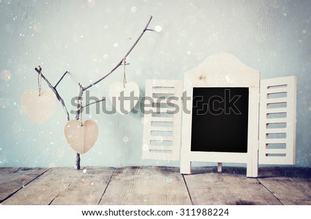 decorative chalkboard frame and wooden hanging hearts over wooden table. ready for text or mockup. retro filtered image
