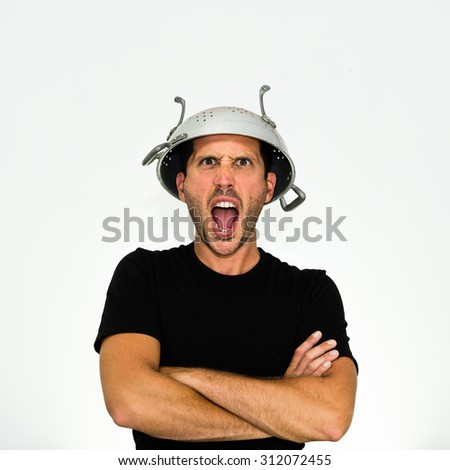 close-up of angry young caucasian man with a colander on his head and arms crossed looking and screaming at you - isolated on white background