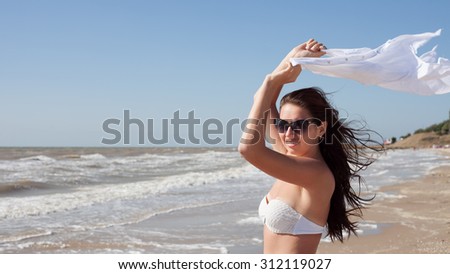 Young smiling girl standing on the seashore and holding a white shirt