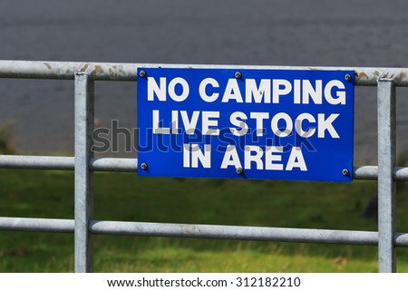 Blue sign fixed to metal  farm gate with the wording No Camping, Live Stock in area 