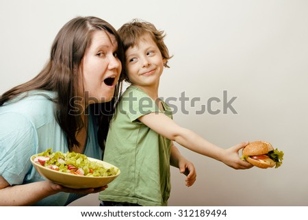 fat woman holding salad and little cute boy with hamburger teasing, real family on white