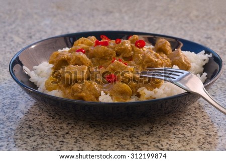 Detailed Picture of typical indian food hot lamb curry with rice and chopped chili served on the deep plate or shallow bowl in the garden on the stone granit table with silver or stainlessteel fork.