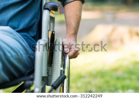 Detail of a man using a wheelchair in a park. Copy-space on the right side Royalty-Free Stock Photo #312242249