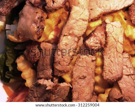 Royalty Free Photograph - Studio Image of A Generous Portion of Juicy and Delicious Pieces of Grilled Sirloin Steak Sitting atop the French Fries and the Fresh Salad Greens.