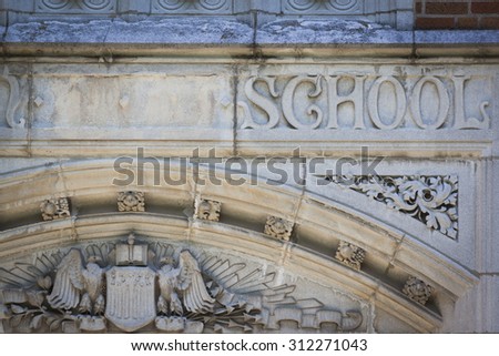 The word School carved into the stone facade of an old schoolhouse.