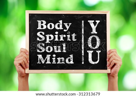 Hands holding blackboard with text You Body Spirit Soul Mind against green blurred background.