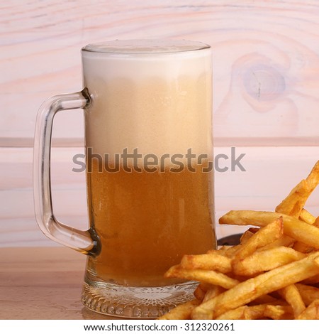 One big glass bocal of light cold delicious beer with white froth and tasty crispy yellow potato fasfood chips on wooden background closeup, square picture