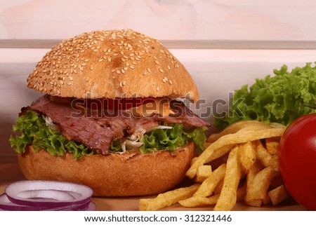 One big tasty appetizing fresh burger of green lettuce red tomato cheese bacon slice meat cutlet violet oinion and white bread bun with sesame seeds on wooden table closeup, horizontal picture