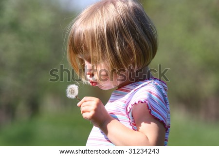 Little girl playing with dandelion flower at the meadow on nice afternoon.