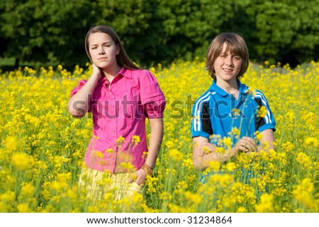 Girl and boy relaxing on meadow full of yellow flowers. Soft focus. Focus on eyes.