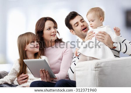 Portrait of happy family sitting at sofa at home while watching cartoon at digital tablet. 
