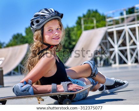 Teen girl in helmet sitting on his skateboard outdoor.
