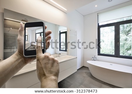 Mobile device with man hands taking picture in  tiled bathroom with windows towards garden