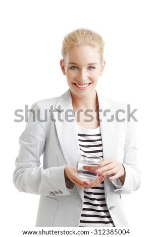 Portrait of smiling young woman standing against white background while holding hand a glass of water. Healthy lifestyle.