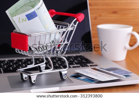 Online shopping. Shopping cart with one hundred euro note on laptop.