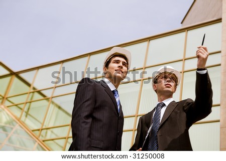 Photo of serious employee pointing at something with confident foreman standing near by