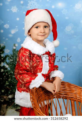 beautiful little boy in a red suit and cap in Christmas decorations is worth about wicker toboggans