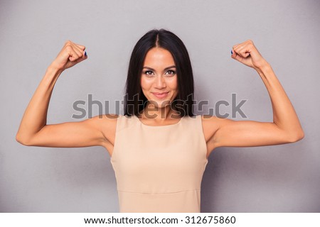 Portrait of a happy elegant woman showing her biceps on gray background Royalty-Free Stock Photo #312675860