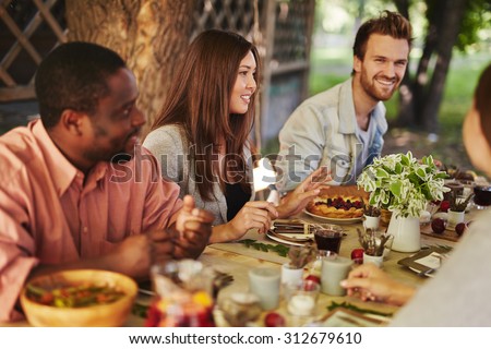 Happy young woman sitting by Thanksgiving table among her friends