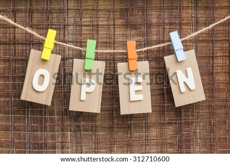 word  open  design by  white letterpress with  box paper  hang on rope by wooden peg over metal net and brown wooden background